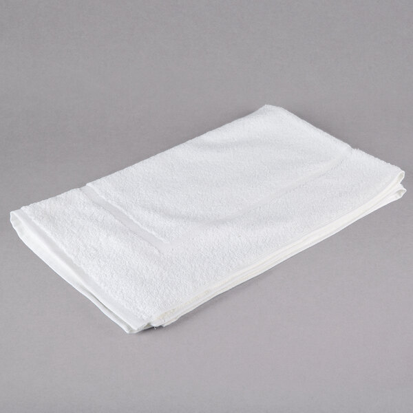 A folded white Oxford Belleeza bath mat on a gray surface.