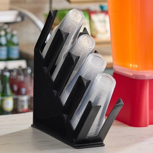 A black four-section slanted countertop organizer holding stacks of clear plastic cups.