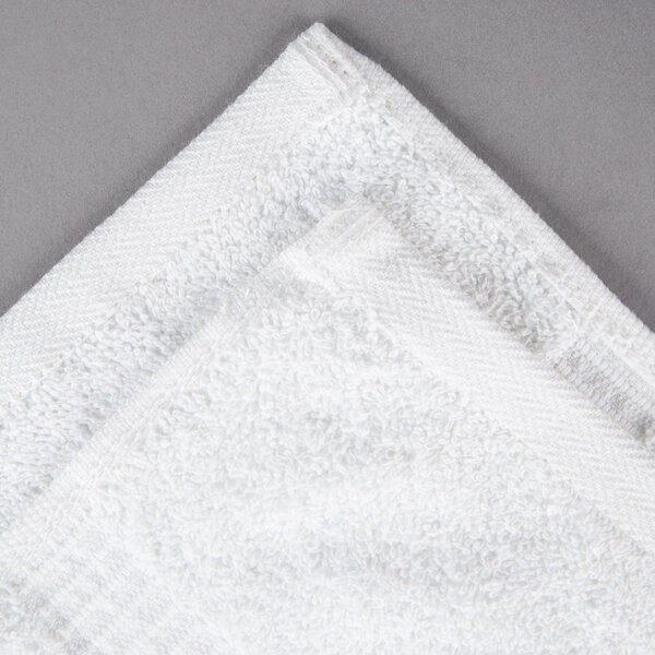 An Oxford Belleeza white hand towel on a gray surface.