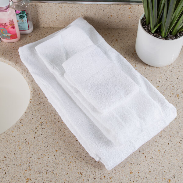 A white Oxford Belleeza bath towel on a counter next to a plant.