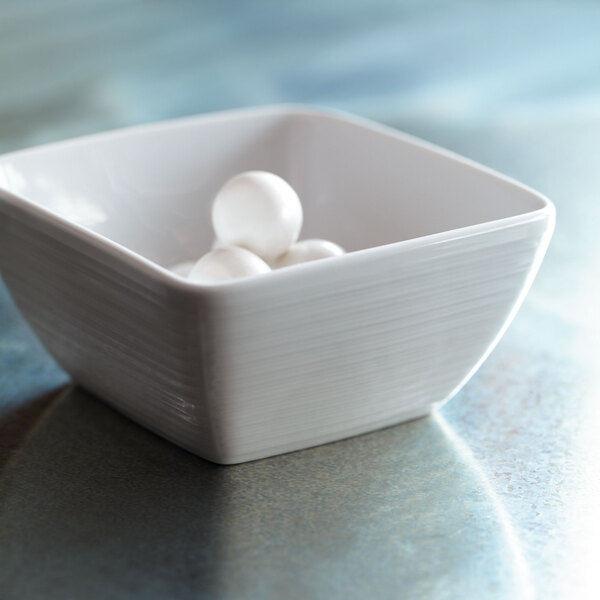 A white Oneida Botticelli square porcelain bowl with white balls in it.