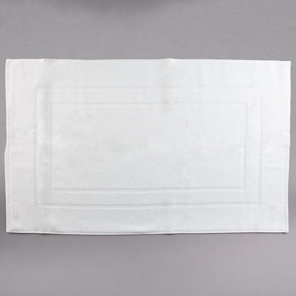 A pack of white Oxford Platinum bath mats with dobby twill hems on a gray surface.
