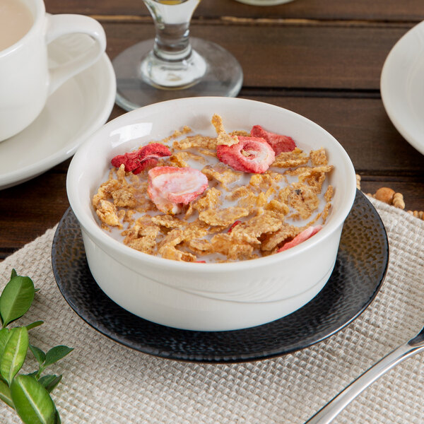 A Oneida cream white china bowl filled with cereal, strawberries, and milk on a table.