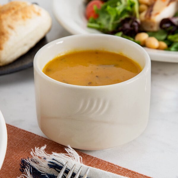 A Oneida Odyssey bouillon cup filled with soup next to a plate of salad.