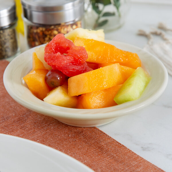 A Oneida cream white china bowl filled with fruit on a table.