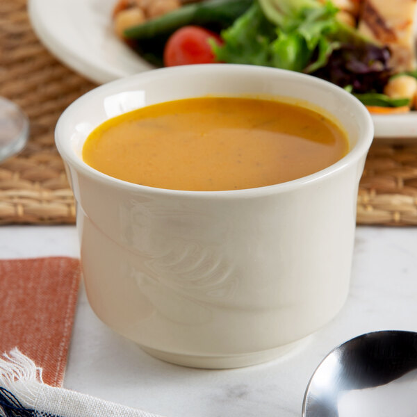 A close up of a Oneida cream white china bouillon cup filled with soup.