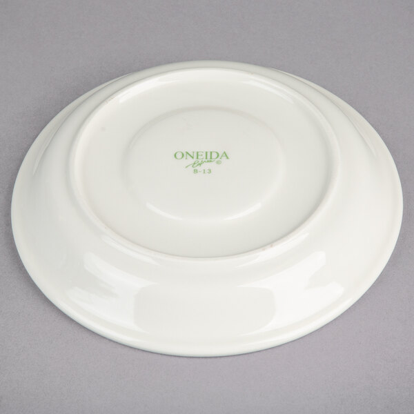 A cream white Oneida Odyssey saucer with green writing that reads "Ocda"