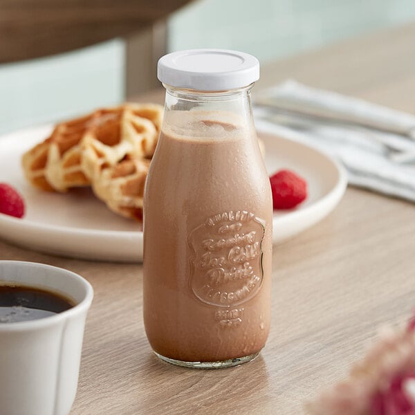 An Acopa glass milk bottle filled with chocolate milk on a plate of waffles.