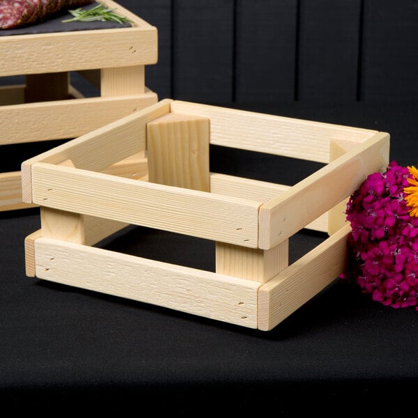 A wooden square display frame used as a riser for a wooden crate with flowers.