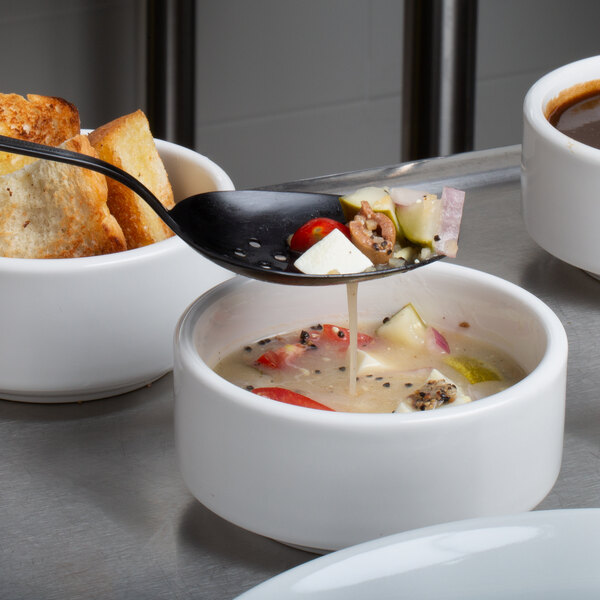 A black Mercer Culinary perforated bowl spoon holding a bowl of tomato soup.