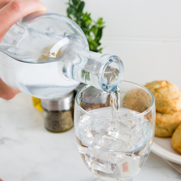 A hand pouring clear liquid from an Anchor Hocking Stockholm Glass Bottle into a glass.