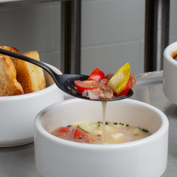 A black Mercer Culinary perforated bowl plating spoon over a bowl of soup.