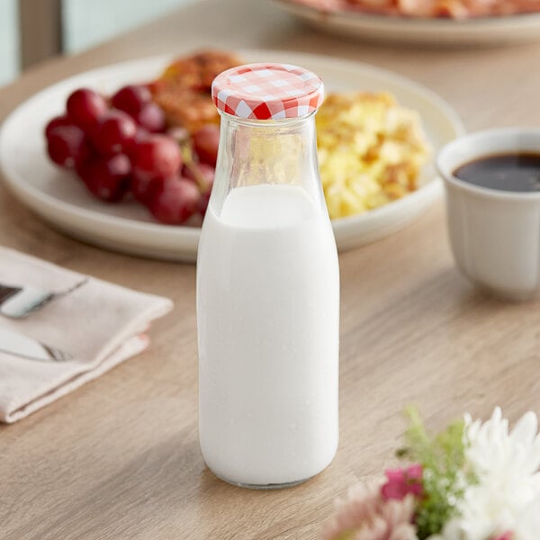 An Acopa glass milk bottle filled with milk on a table.
