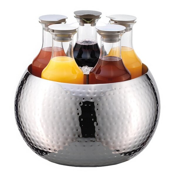 A Frilich stainless steel bowl with six Frilich glass carafes filled with juice and soda on a table.