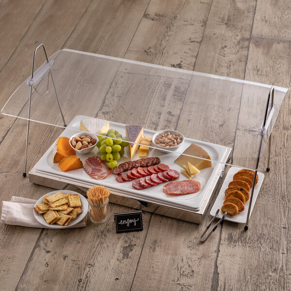 A rectangular Frilich portable sneeze guard over a tray of food on a table.