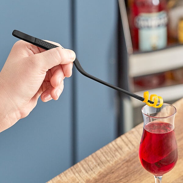 A hand holding a Mercer Culinary black offset tip plating tong over a glass of red liquid with a spiral.