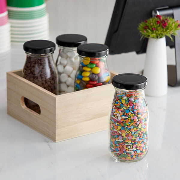 Acopa glass milk bottles filled with a variety of candies in wooden crates.
