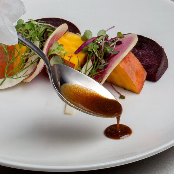 A Mercer Culinary stainless steel plating spoon with sauce on a plate.