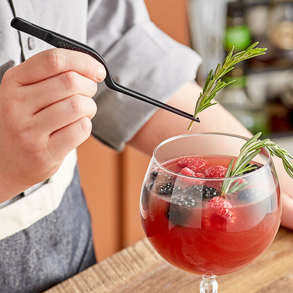 A chef using Mercer Culinary black offset tip plating tongs to add berries and a rosemary leaf to a red drink.