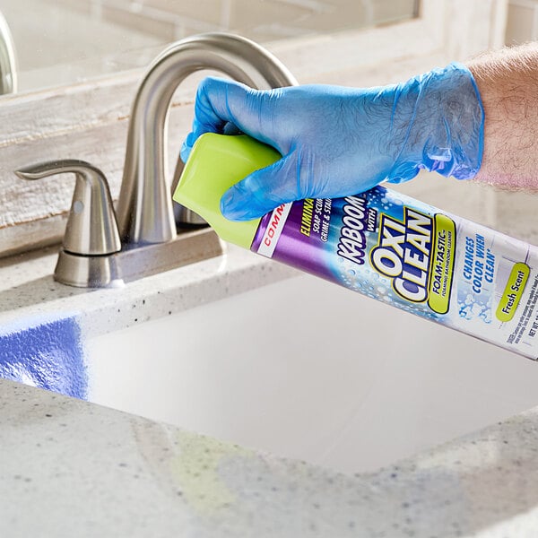 A person in blue gloves spraying Kaboom Foam-Tastic bathroom cleaner.