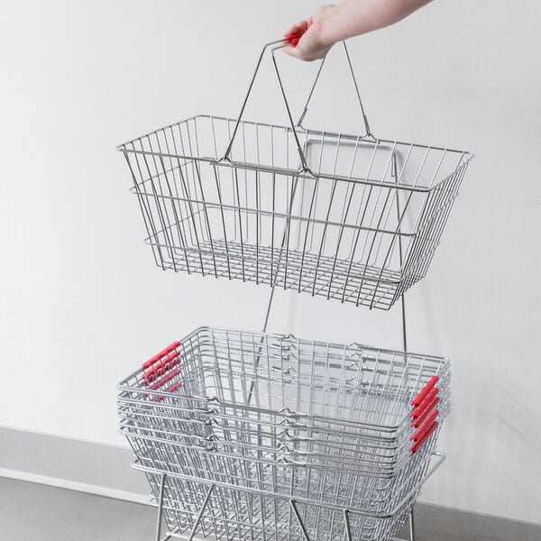 A hand holding two Regency chrome grocery shopping baskets with red handles.