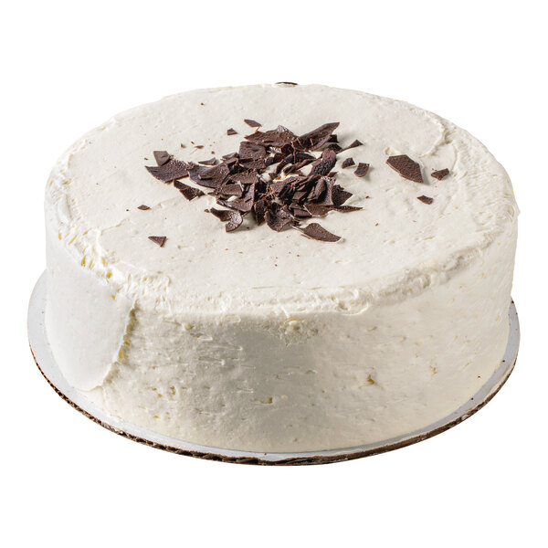 A round cake with white frosting and chocolate shavings on top, displayed on a cake board.