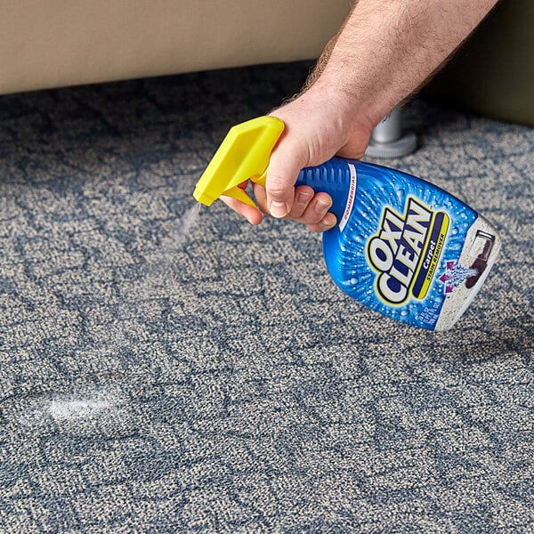 A person holding a spray bottle of OxiClean Carpet Stain Remover spraying the floor.