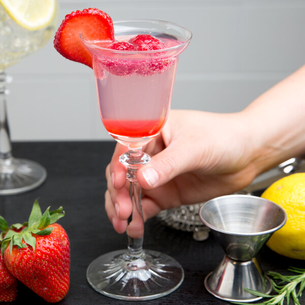 A person holding a Libbey cocktail glass of pink liquid with a slice of strawberry.