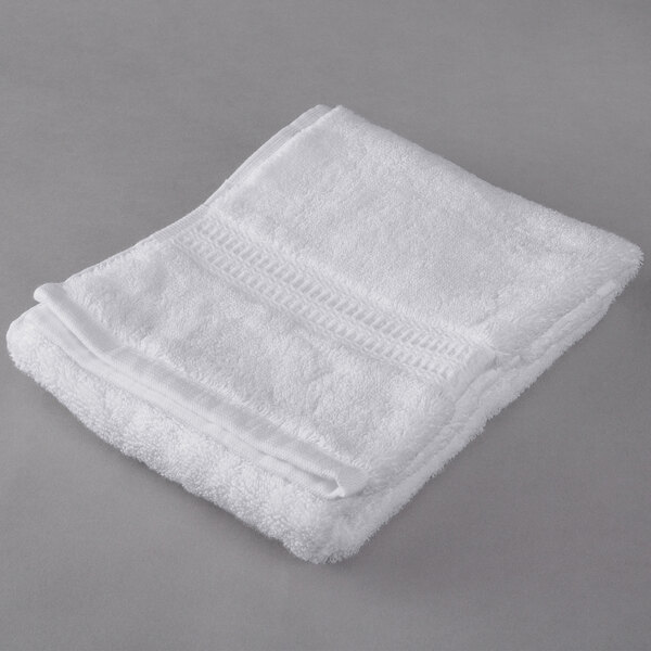 An Oxford Reserve white hand towel with a dobby border folded on a gray surface.