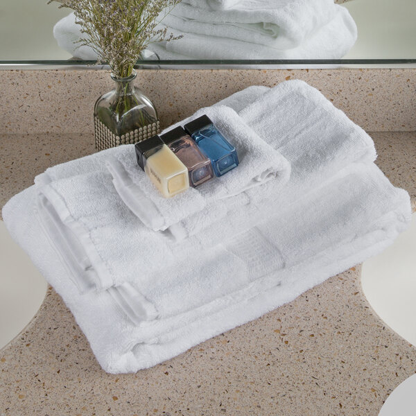 A stack of white Oxford Reserve wash cloths with a bottle of lotion on top.