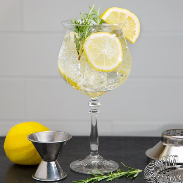 A Libbey gin and tonic glass with lemon slices and rosemary sprigs in it.