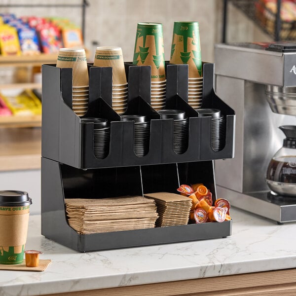 A black 11-section countertop organizer holding cups, lids, napkins, and coffee creamers.