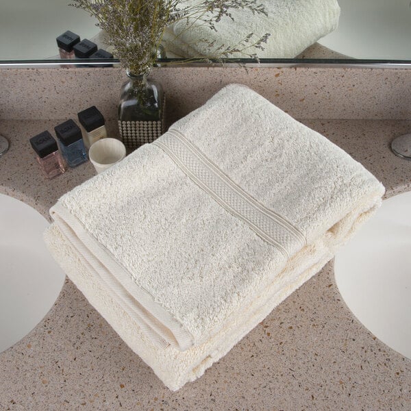 A white Oxford Vicenza Avorio bath towel on a bathroom counter top with a vase of flowers.