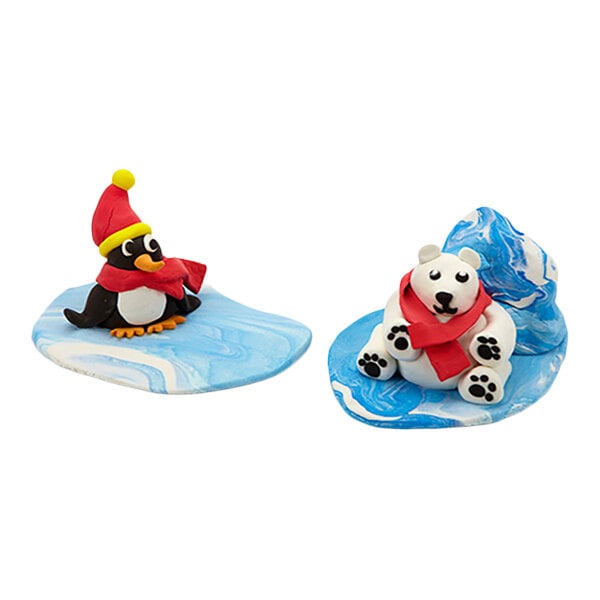 Two small clay figures, one of a penguin wearing a red hat and scarf and the other of a polar bear with a red scarf, are sitting on blue and white marbled bases.
