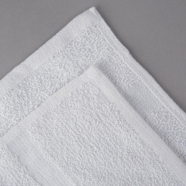An Oxford Gold white bath towel with cam border on a gray surface.