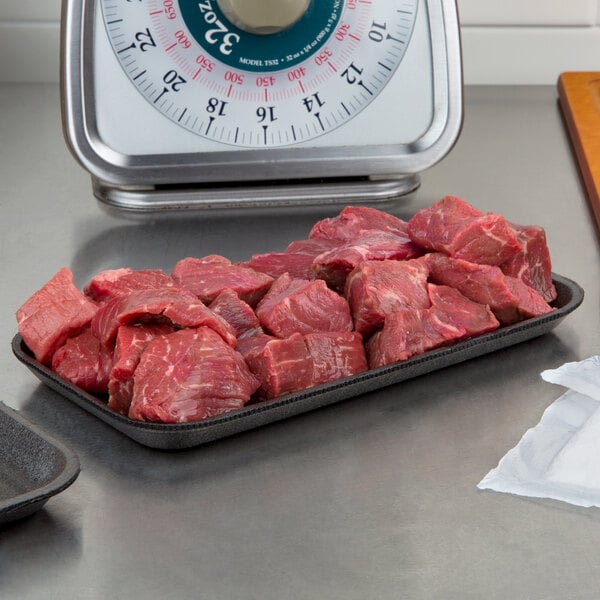 A black CKF foam meat tray on a counter with raw meat.