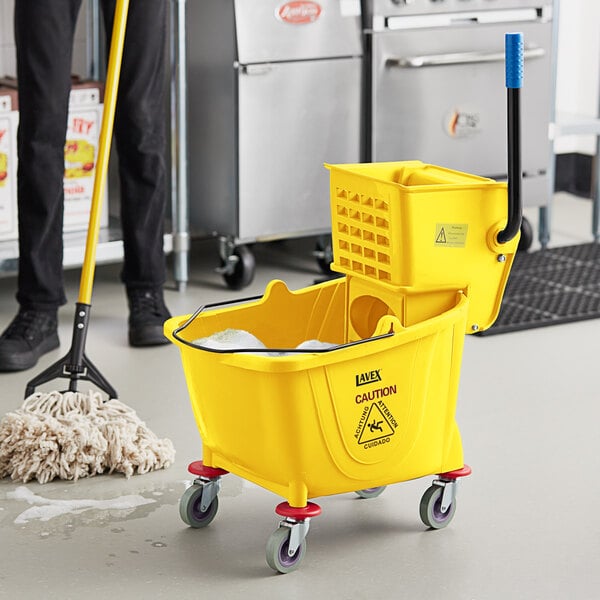 A man using a yellow Lavex mop to clean a floor with a yellow Lavex mop bucket.