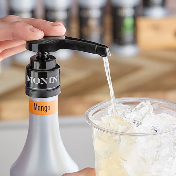 A hand using a Monin concentrated flavoring pump to pour liquid into a glass of ice.