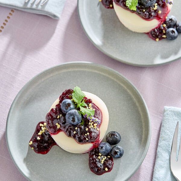 A dessert topped with blueberry sauce, fresh blueberries, and a mint garnish on a gray plate.