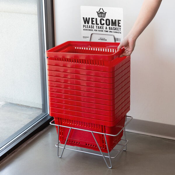 A stack of red plastic grocery market shopping baskets with plastic handles in a metal holder.