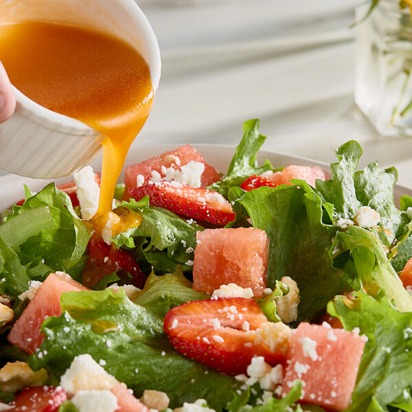 Monin Watermelon Concentrated Flavor being poured over a watermelon salad.