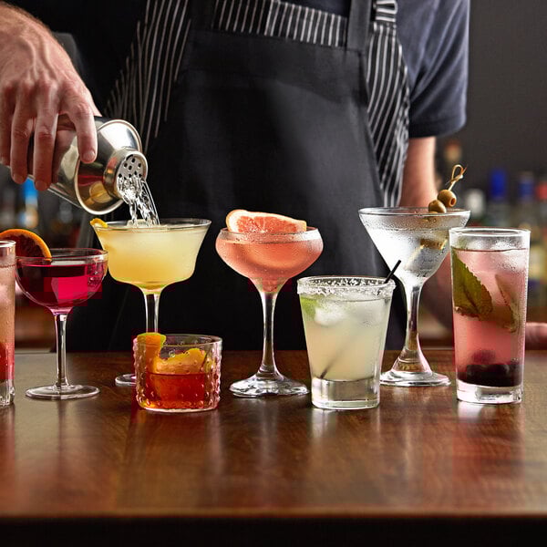 A bartender pouring red liquid into an Acopa Hobnail rocks glass on a table in a cocktail bar.