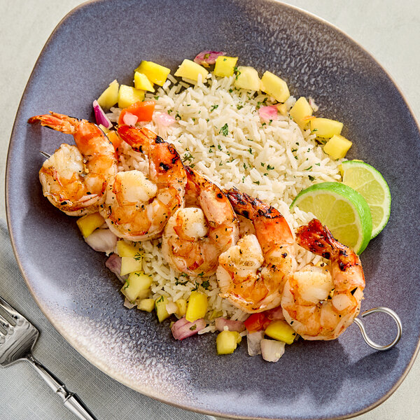 A plate of grilled shrimp skewers served over rice with diced vegetables and garnished with lime slices.