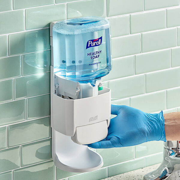 A person in blue gloves using Purell Healthy Soap dispenser.