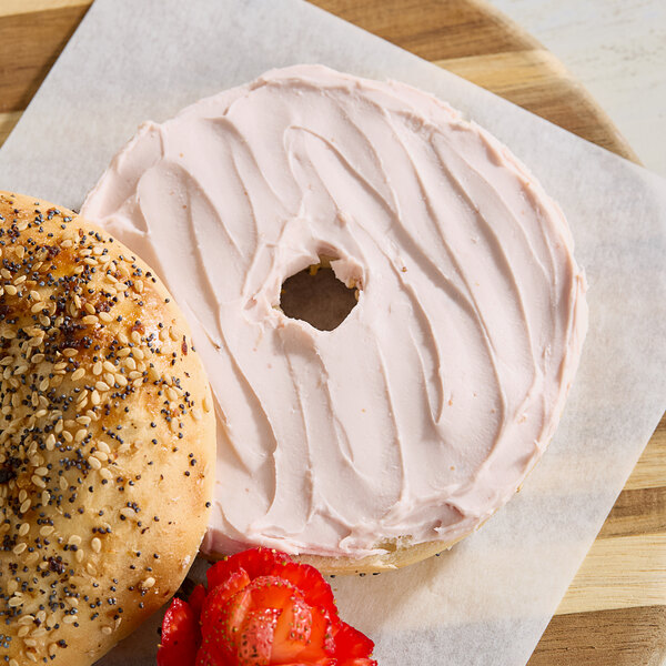 A Monin Strawberry bagel with cream cheese and a strawberry on a wooden surface.