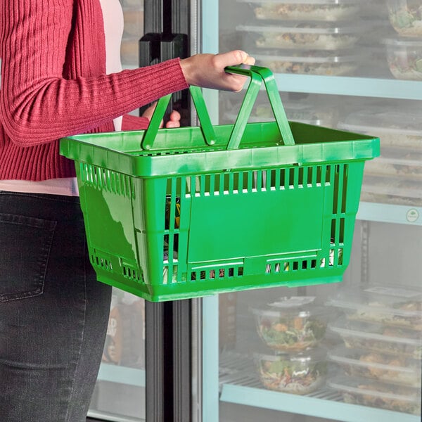 A green plastic grocery market shopping basket with handles being carried by a person.
