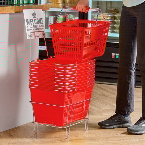 A stack of red plastic grocery market shopping baskets with metal handles, placed on a metal stand with a sign.