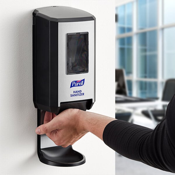 A person using a Purell manual hand sanitizer dispenser on a wall