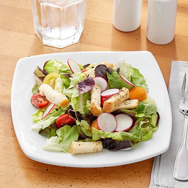 A plate of salad with a fork and knife on a white Acopa square plate.