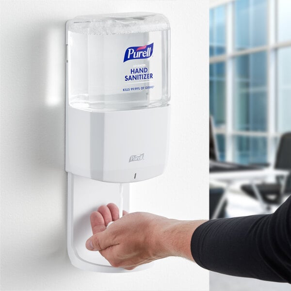A person using a white Purell hand sanitizer dispenser.